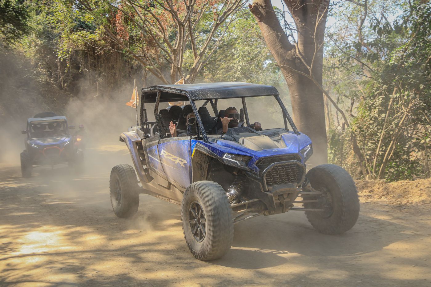 Polaris RZR driving dusty trails surrounded by nature.