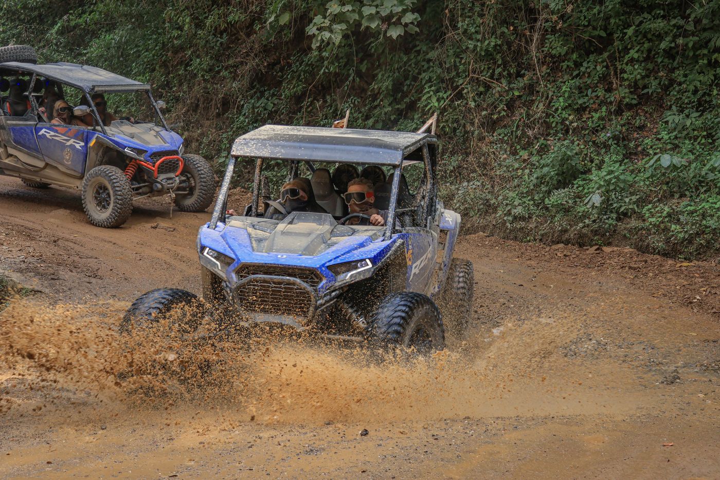 Polaris RZR splashing through a muddy puddle during an off-road tour.